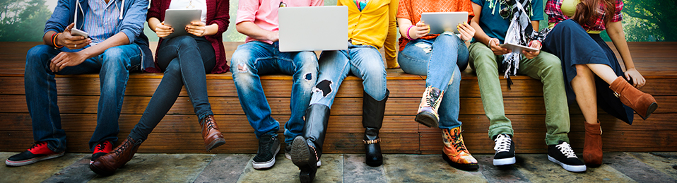 Grupo de estudiantes sentados en un banco mientran usan tablets, móviles y un ordenador portátil